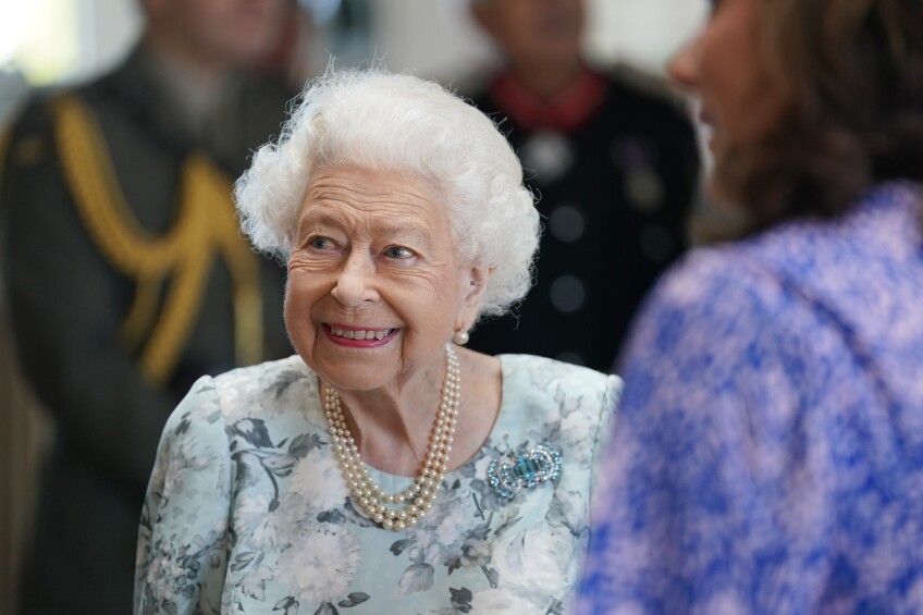 Queen Elizabeth II smiles while looking towards her right, wearing a blue floral dress