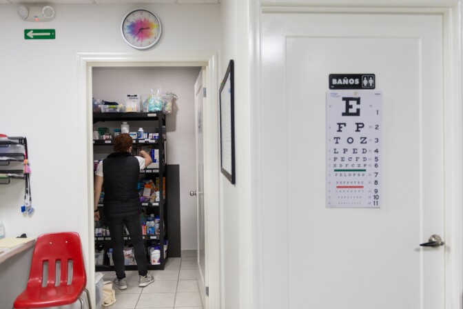 A volunteer reaches for something on a shelf of supplies. Outside, is a door to the restroom and a bright red chair.