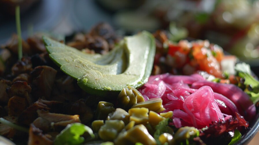 A vegetable bowl full of freshly grilled corn, black beans and cubed summer squash topped with bright-pink pickled onions, tomatoes and sliced avocado.