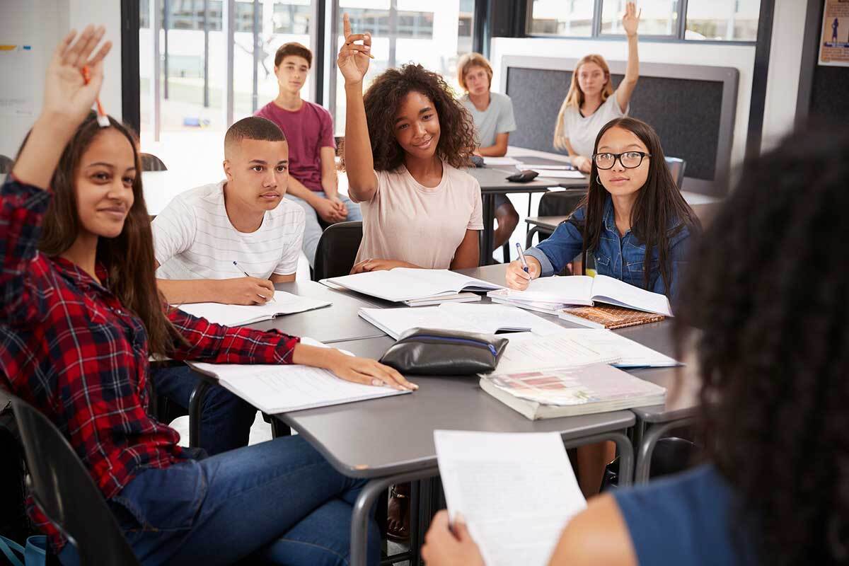 Two tables filled with seven students facing a teacher in the foreground.