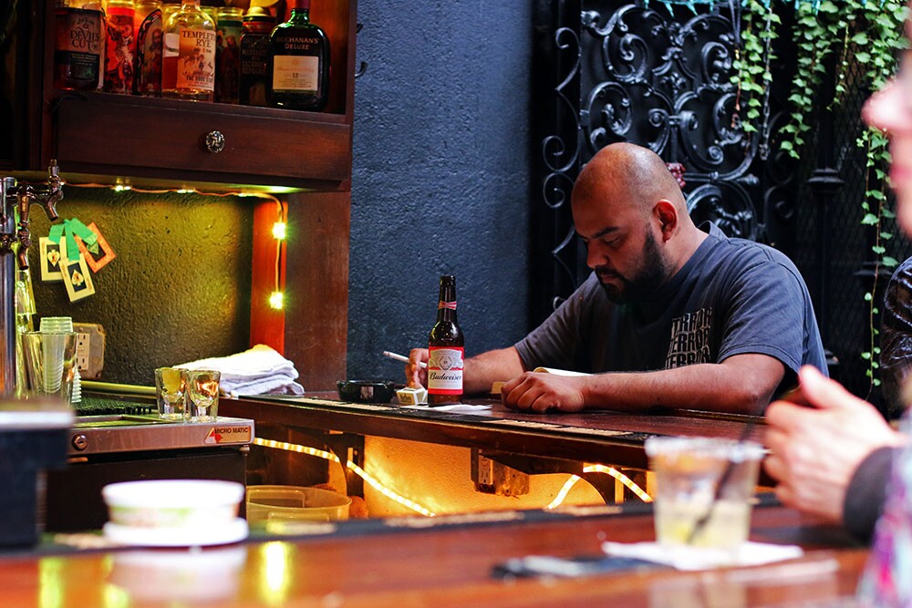A man sits at the La Cita bar with a cigarette and a Budweiser.