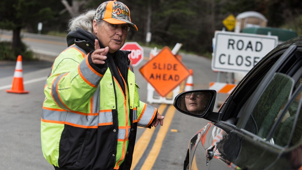 Caltrans contractor Arleen Guzzie gives directions at the Ragged Point road closure. | Photo: Brian van der Brug/Getty Images