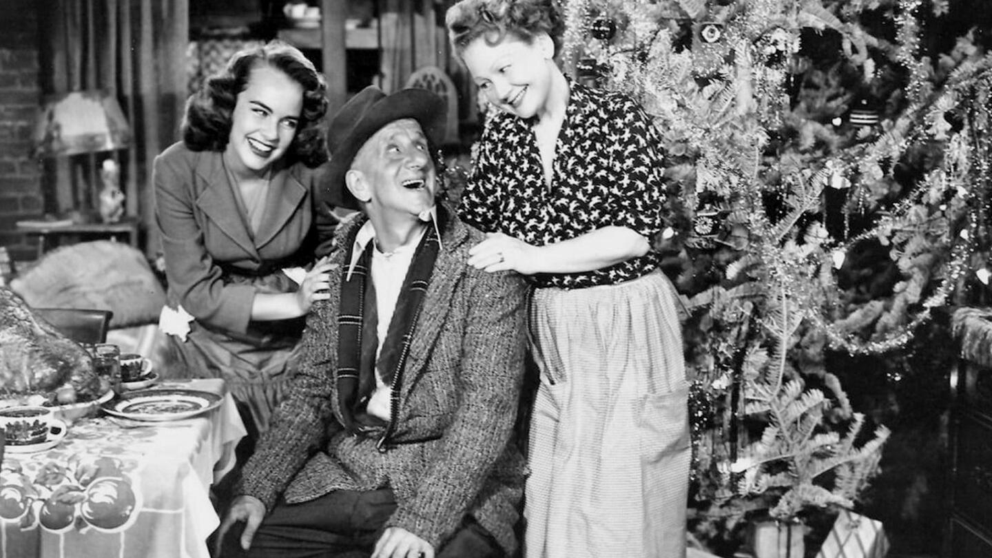 Family members look at each other with smiles in a home decorated for the holidays.