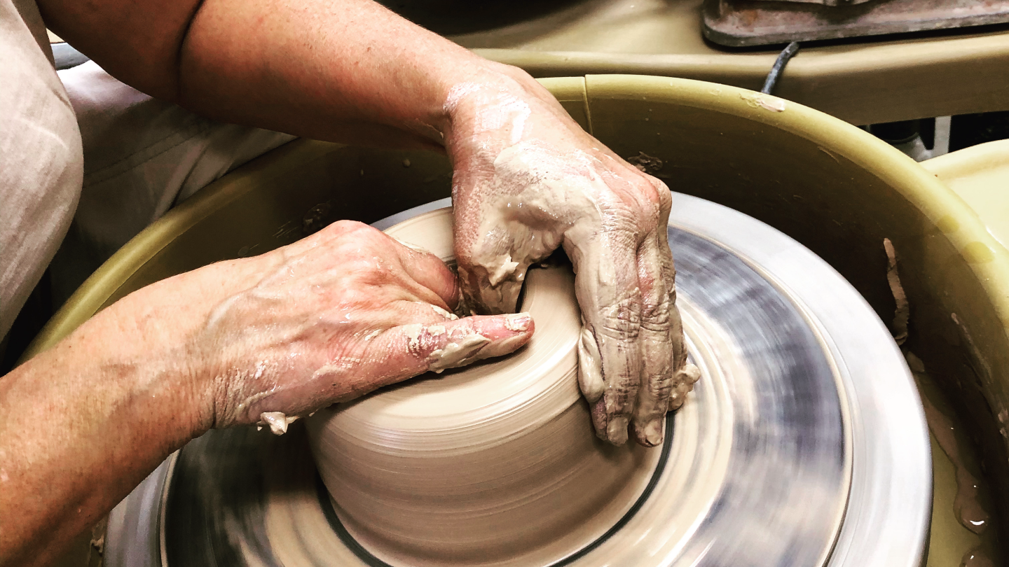 Two hands a centering clay on a potter's wheel.