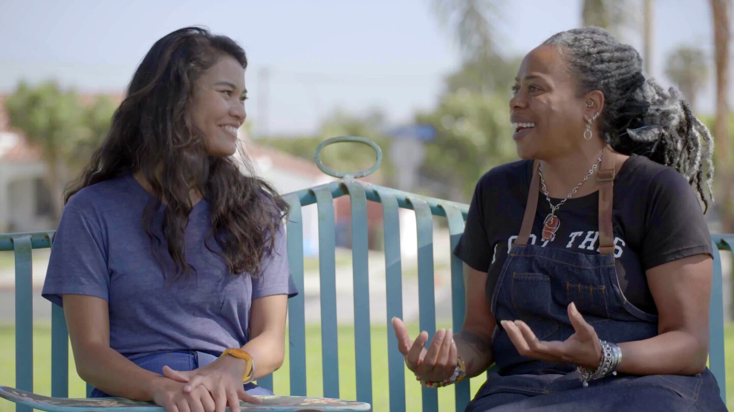 A young Filipina American woman and an older African American woman sit in the bench chatting.