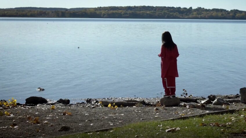 A Native American woman stands at the edge of a lake