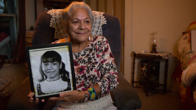 An Indigenous woman holds up a framed photograph of a little girl. | From "Independent Lens: Dawnland"