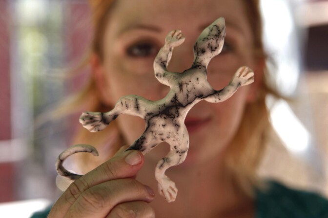 A woman holds up a gecko-shaped ceramic piece.
