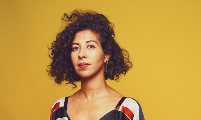 Filmmaker Assia Boundaoui stands in front of a yellow backdrop.