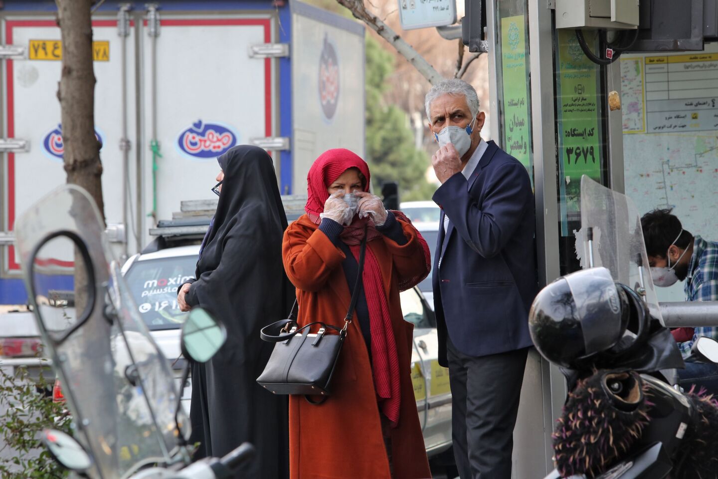 People wearing protective masks wait along the side of a street in the Iranian capital Tehran on February 24, 2020