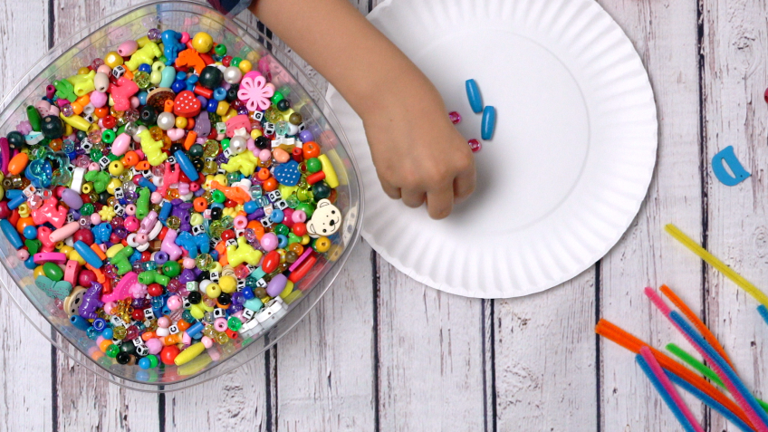 A small child's hand sorts colorful pairs of beads by color.