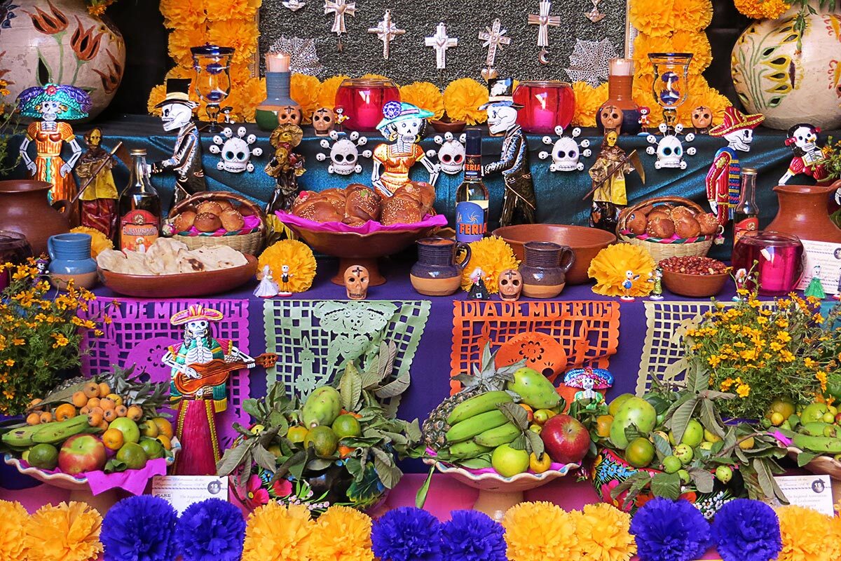 A Day of the Dead altar is covered in flowers, bread, decorative skulls and intricately cut brightly colored paper.