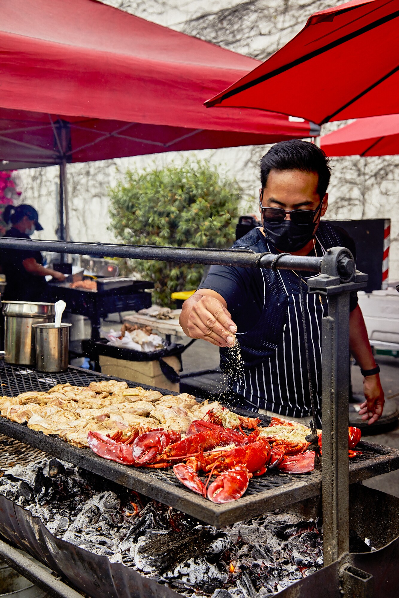 Johnny Angeles seasons lobsters at Lobsterdamus. He stands beneath red umbrellas.