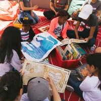 Children sitting on a mat reading books with parents and caregivers. | PBS SoCal