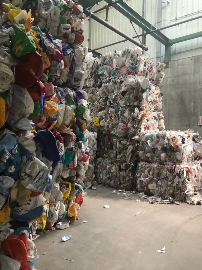 Bales of multicolored recovered plastic are piled several feet high in a warehouse.