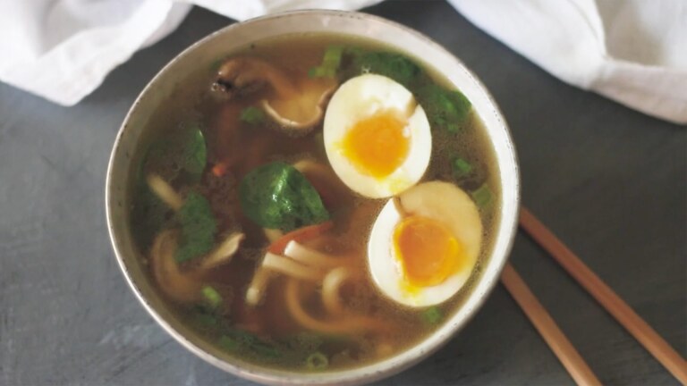 View of soup bowl from the top with brown broth and a boiled egg cut in half
