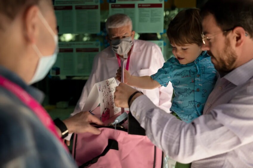 Election workers collect a ballot from a man holding a child in his arms.