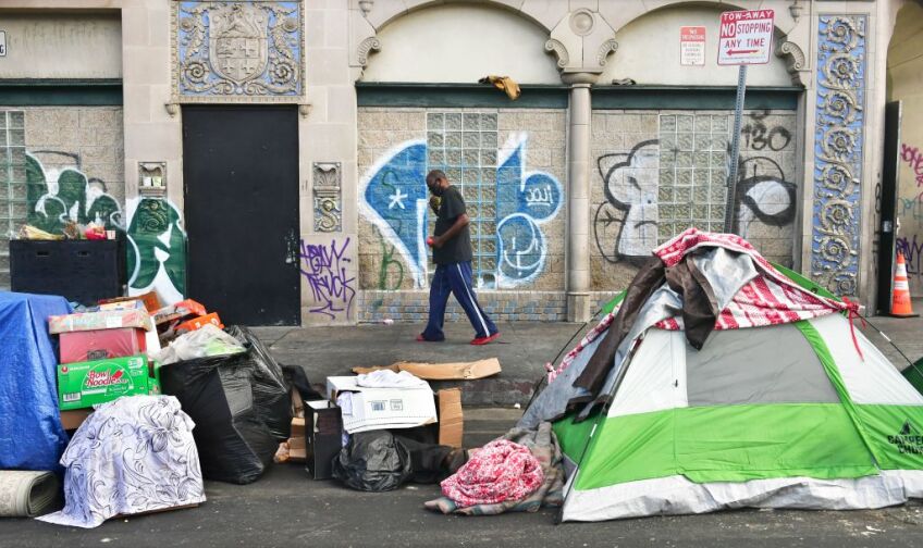 A man walks past tents housing the homeless on the streets in the Skid Row community of Los Angeles, California on April 26, 2021.