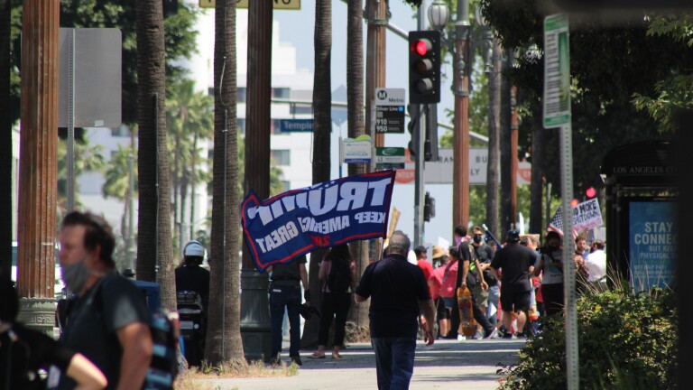Man with "Trump 2020" flag walks down street, towards other protestors on May 1 in Downtown L.A. | Karen Foshay