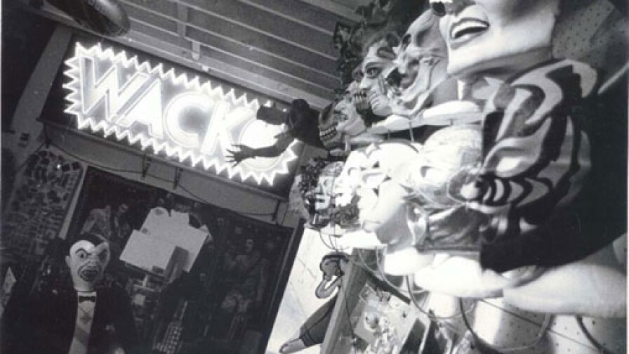 A neon sign that reads "WACKO" and walls covered with face masks adorn the interior of the store.