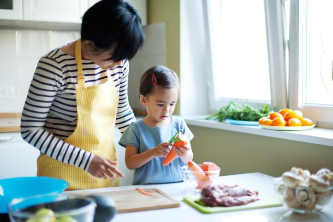 Mother working with small child to teach her how to use a vegetable peeler. cooking