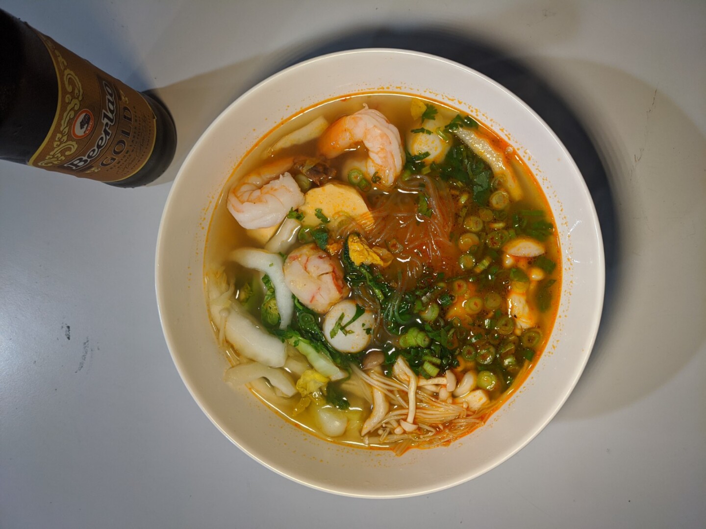 An overhead shot of a bowl of sukiyaki, a mung bean noodle soup filled with various herbs, mushrooms, shrimp and noodles.