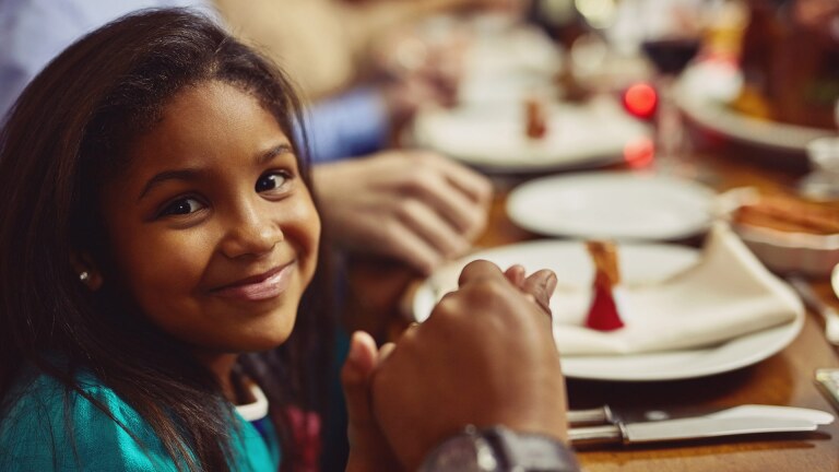 Portrait of an adorable little girl holding hands in prayer with her family before having a meal together. iStock