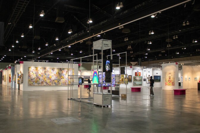 NFT-backed digital art on display on LED screen mounted onto a metal pipe structure in the middle of a convention center. Around the exhibition are various booths and gallery walls displaying pieces from other artists from around L.A. and the world.