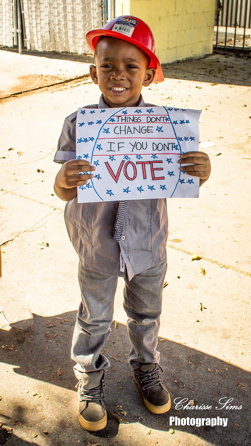 A little boy holds up a sign asking people to vote.