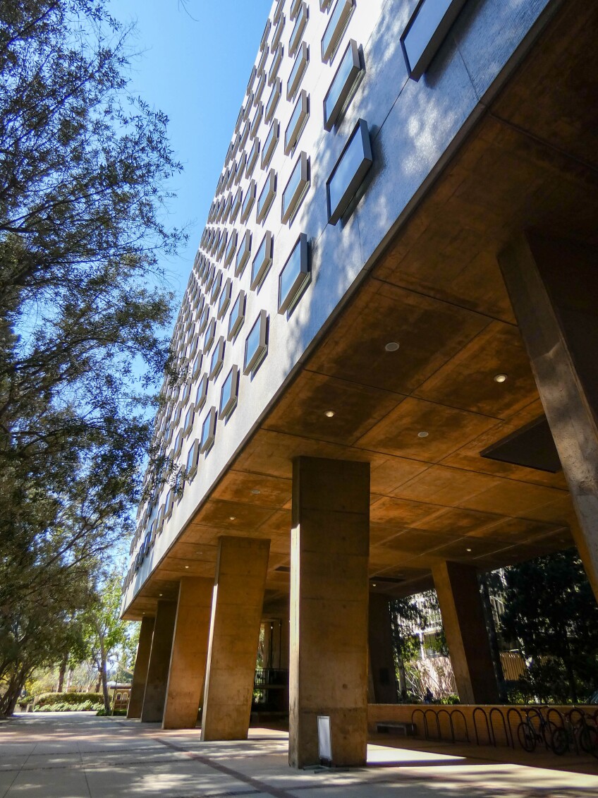 The exterior of a building featuring large pillars and small, uniform square windows spread out evenly across the face of the building. 