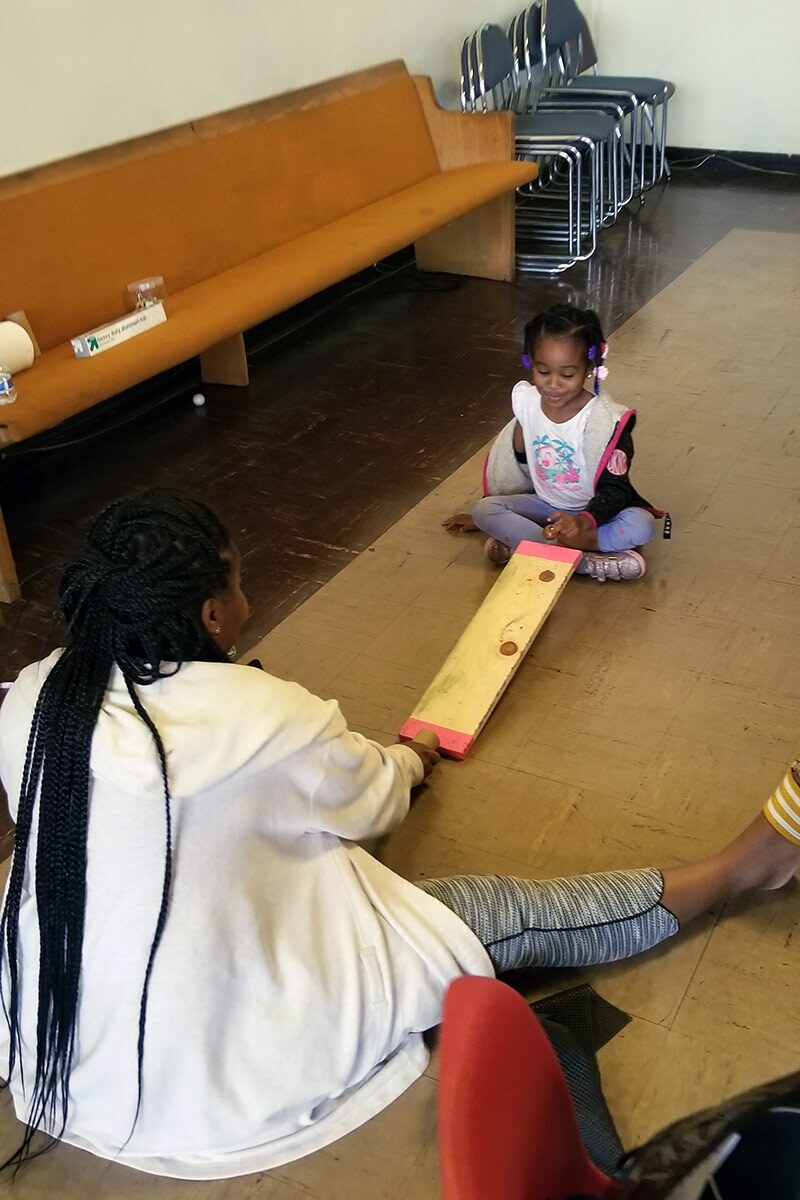A small ramp on a carpet made out of a wood slat and propped up with two small water bottles