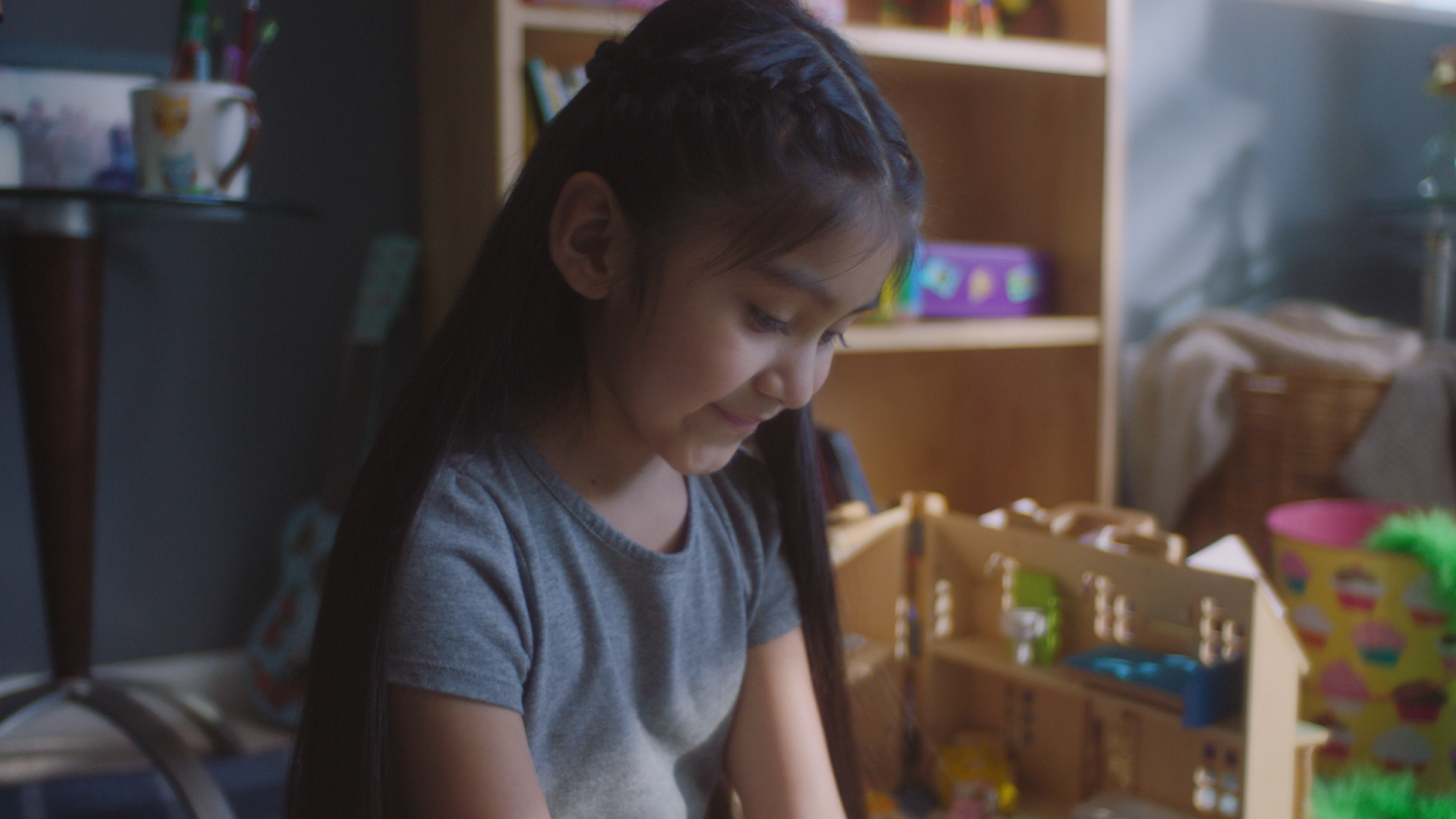 a small girl looks down as she cleans toys off the floor