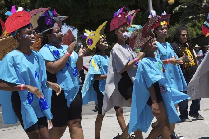 Young people wearing blue tunics and colorful helmets walk at the 2017 edition of the Day of the Ancestors: Festival of Masks. | Photo by Sahra Sulaiman, Courtesy of LA Commons