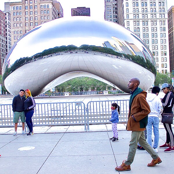 People walking and posing in front of the "Cloud Gate" sculpture in Chicago.