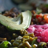 A vegetable bowl full of freshly grilled corn, black beans and cubed summer squash topped with bright-pink pickled onions, tomatoes and sliced avocado.