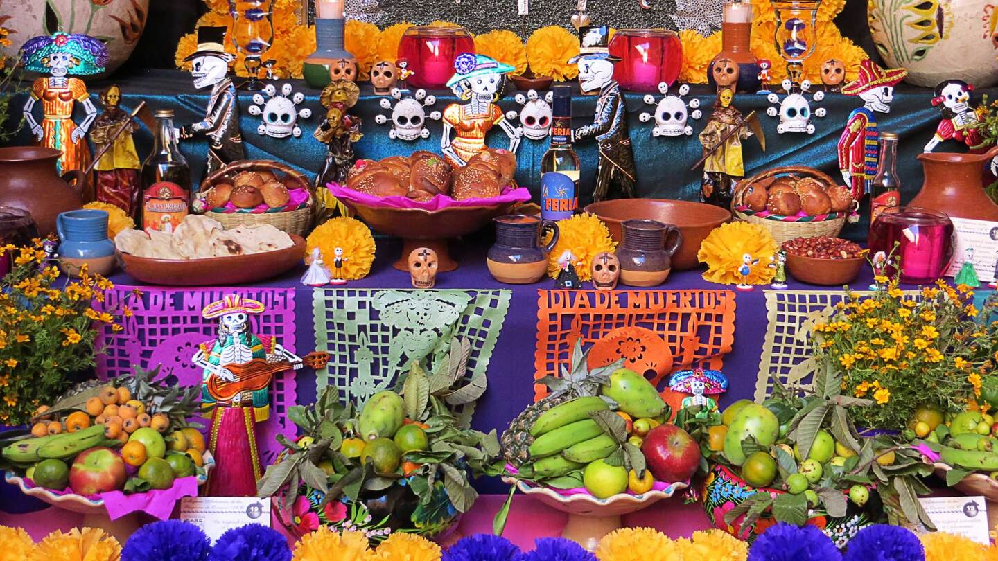 A Day of the Dead altar is covered in flowers, bread, decorative skulls and intricately cut brightly colored paper.
