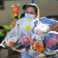 Beatrice Lopez walks out with sports items and meal bags distributed by LA84 Foundation and LAUSD at Grab and Go center at Thomas Alva Edison School.