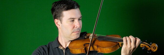 Nathan Cole plays the violin in front of a green wall. | Courtesy of Nathan Cole