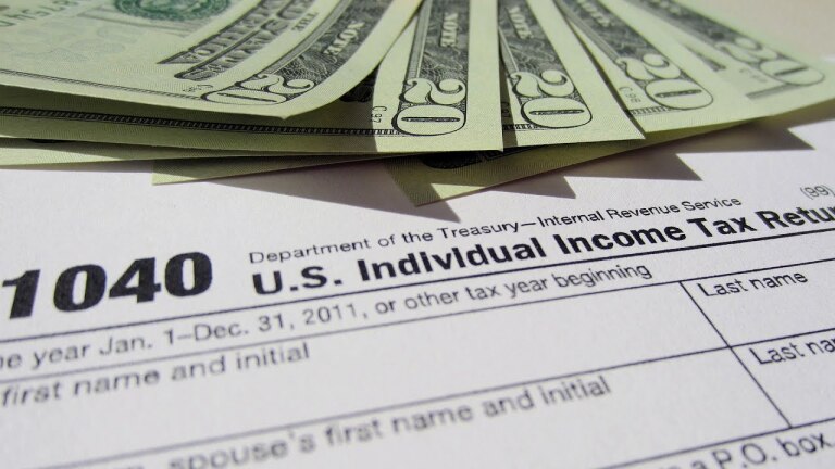 Twenty-dollar bills fanned across U.S. income tax forms. | Democracy Now