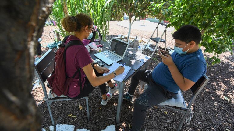 East College Prep High School senior Jocelyn Hernandez follows a remote Advanced Placement (AP) Calculus class as her cousin plays with his phone while sitting in a community garden near her home, August 14, 2020 Boyle Heights. | ROBYN BECK/AFP via Getty