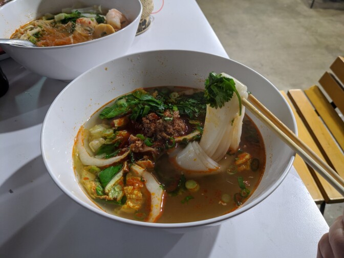 A bowl of khao soi, rice noodle in a clear pork broth underneath sautéed fermented soybeans, dried chilis and minced pork.
