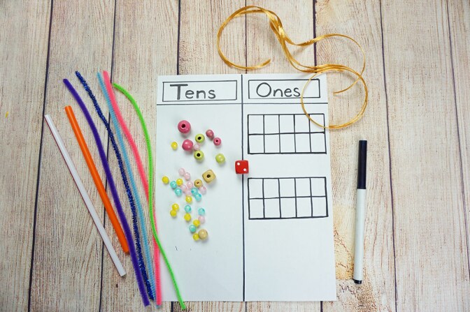 A sheet of paper divided into two columns with the headings "tens" and "those" with beads, pipe cleaners, pieces of string and a marker on it.