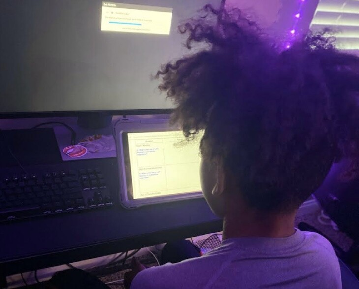 Photo of a young boy with black curly hair looking at a computer with purple light around him.