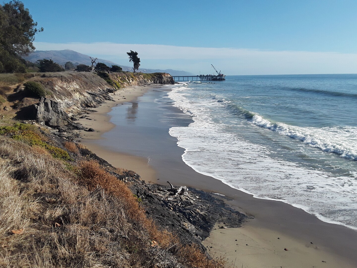 A wave pushes in on the shore of Carpinteria State Beach as a small hill of black tar builds right at the start of the beach.