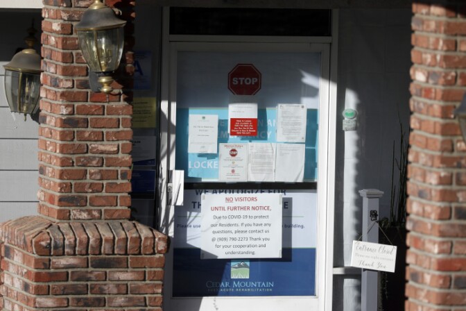 Warning notices are posted on a door at the Cedar Mountain Post Acute nursing facility in Yucaipa, after a COVID-19 outbreak there. | Chris Carlson/AP