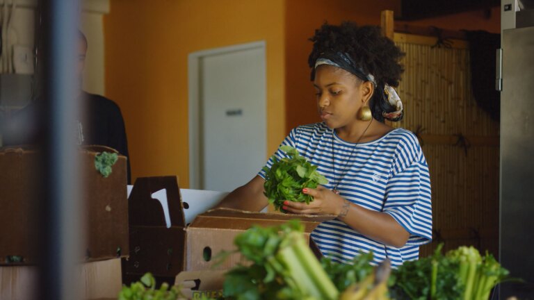 Vegan grocer Olympia Auset assembles a box of fresh produce for a client. | Still from "Broken Bread"