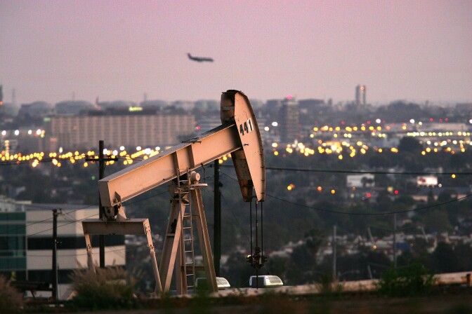 An oil rig stands at a site while a plane lands in the distance.