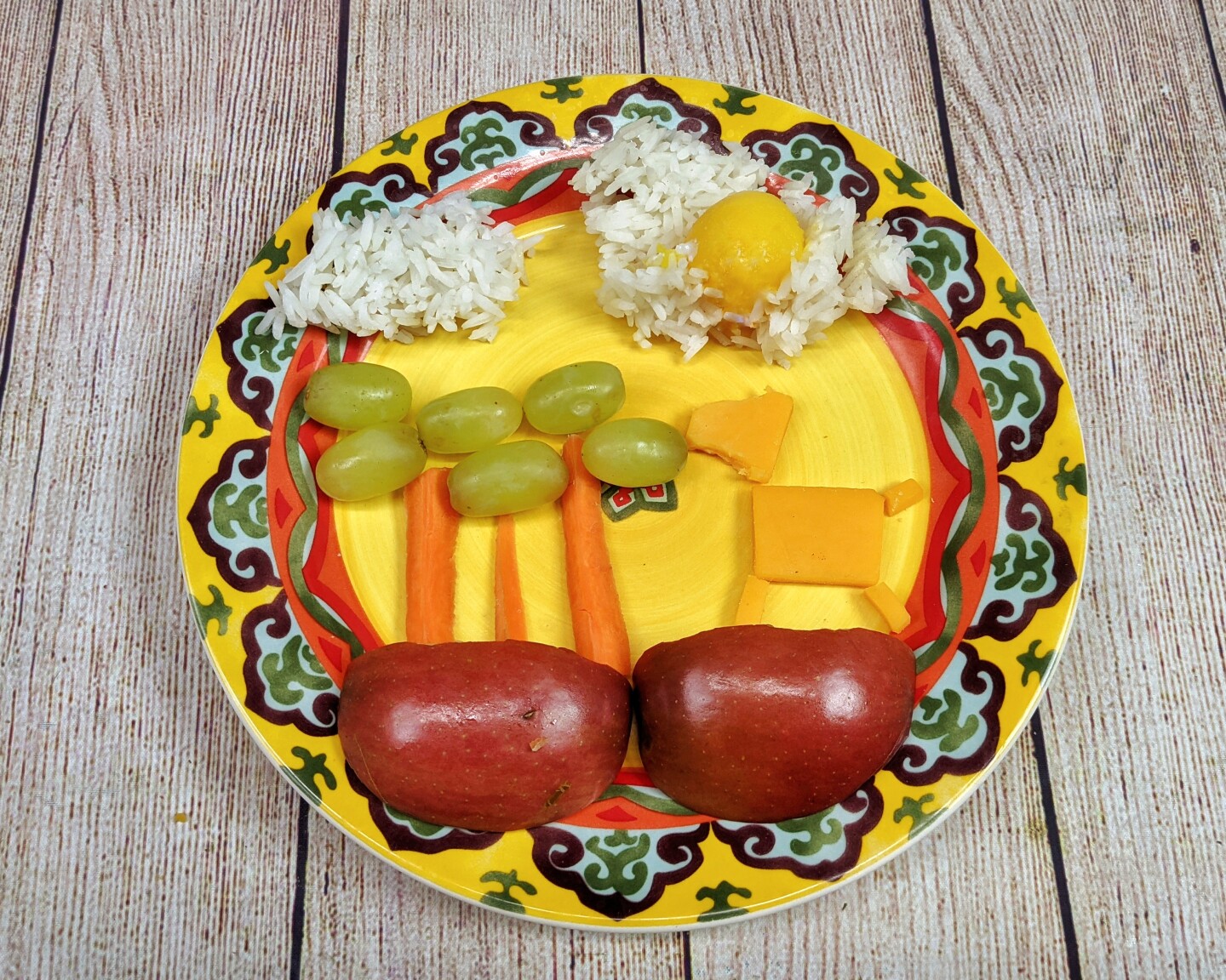cheese, apples, carrot slices and grapes are arranged in the shape of a cheese farm animal eating grapes from carrot stick trees.