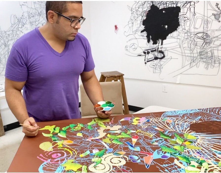 Artist David Rios stands over one his works in his art studio.