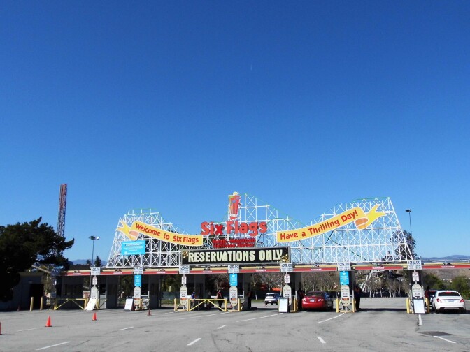 The entrance to Six Flags Magic Mountain with signage that reads, "Welcome to Six Flags. Have a thrilling day!" Another sign reads, "Reservations Only."